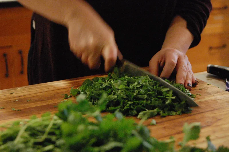 Hands chopping fresh herbs on a wooden cutting board
