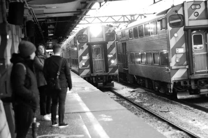 Commuters on a snowy platform beside a passenger train, in black and white